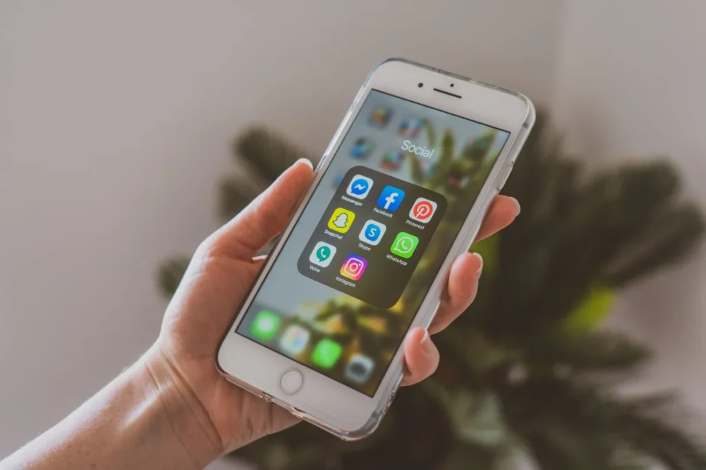 Kafe masasındaki iPhone’da beta profili yükleyen kişi ve yanında açık bir dizüstü bilgisayar